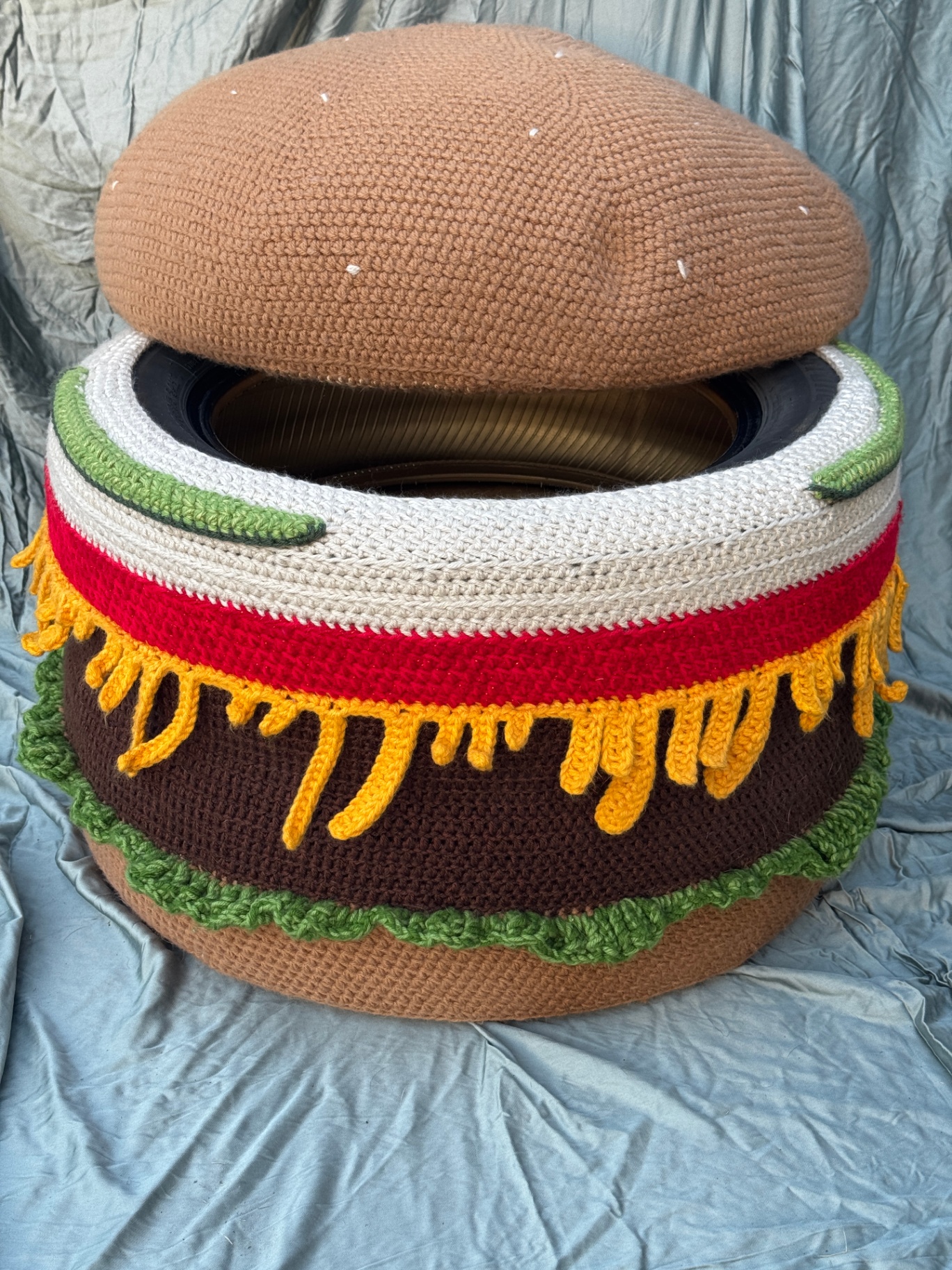 The burger ottoman on a gray backdrop with the bun lid resting on top.